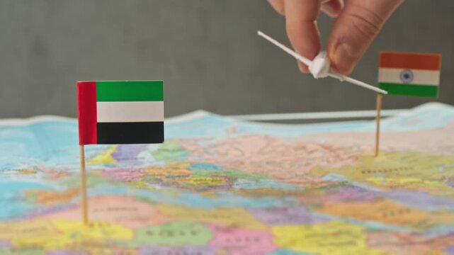 Toy airplane flying from India to United Arab Emirates above colorful world map, symbol shopping tourism, luxury holidays, business trips and busy air route between countries.