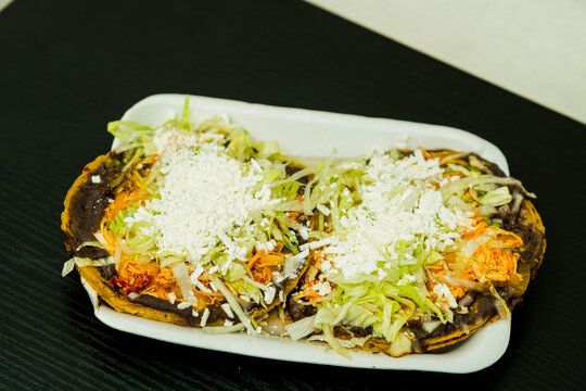 Sopes de tinga de pollo, a Mexican dish with a corn base, a bed of beans, shredded chicken breast, lettuce, and cheese
