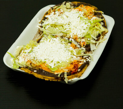 Sopes de tinga de pollo, a Mexican dish with a corn base, a bed of beans, shredded chicken breast, lettuce, and cheese