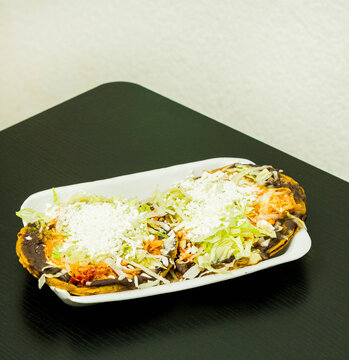Sopes de tinga de pollo, a Mexican dish with a corn base, a bed of beans, shredded chicken breast, lettuce, and cheese