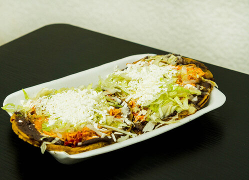 Sopes de tinga de pollo, a Mexican dish with a corn base, a bed of beans, shredded chicken breast, lettuce, and cheese