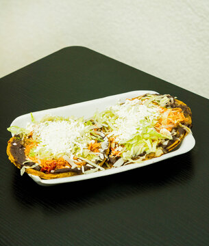 Sopes de tinga de pollo, a Mexican dish with a corn base, a bed of beans, shredded chicken breast, lettuce, and cheese