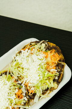 Sopes de tinga de pollo, a Mexican dish with a corn base, a bed of beans, shredded chicken breast, lettuce, and cheese