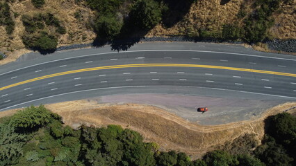 Vista aérea superior de carretera asfaltada sinuosa con doble línea amarilla, rodeada de colinas...