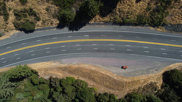 Vista a&eacute;rea superior de carretera asfaltada sinuosa con doble l&iacute;nea amarilla, rodeada de colinas y bosque.