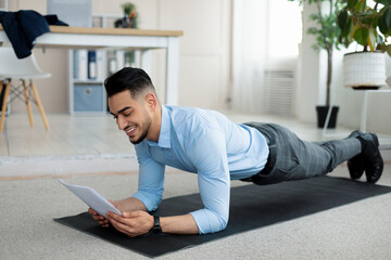 Workplace fitness. Millennial Arab company employee exercising on yoga mat, standing in elbow plank...