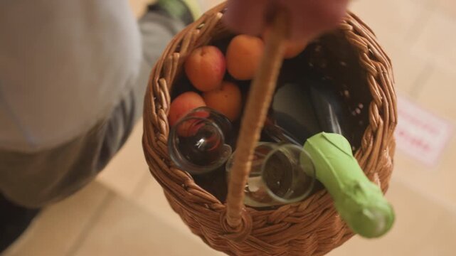 overhead view of wicker basket carried by shopper walking on tiled floor, basket filled with oranges, glass bottle, reusable bag, casual sneakers visible, warm soft light, intimate everyday market