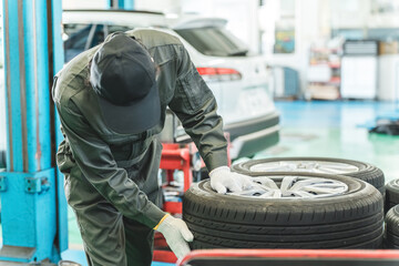 Male mechanic carrying tires at an auto repair shop (physical labor, hard work, heavy, back pain) © buritora