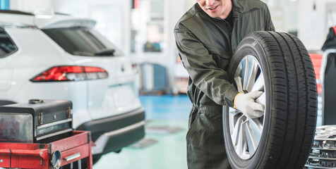 Male mechanic carrying tires at an auto repair shop (physical labor, hard work, heavy, back pain) © buritora