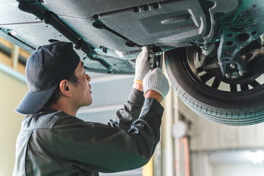 A male car mechanic performing maintenance, inspection and work under a vehicle going up on a lift