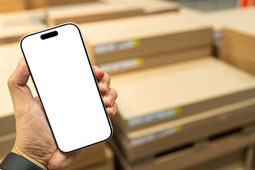 Man hand holding smartphone with blank white screen in blurred warehouse background, AI logistics and inventory management concept. Supply chain logistics, smart warehousing, and online shopping.