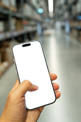 Man hand holding smartphone with blank white screen in blurred warehouse background, AI logistics and inventory management concept. Supply chain logistics, smart warehousing, and online shopping.