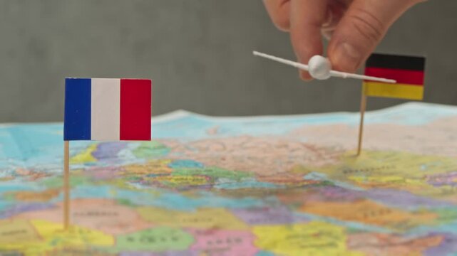 Toy airplane flying from Germany to France above colorful world map, symbol city breaks, business trips, wine tourism and frequent flights between countries.