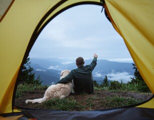 Man and Dog Sharing a Tent View During Camping. Pets + Human Bonding. A man and his dog huddled together inside an open tent looking out at a vast misty mountain landscape in the early morning.
