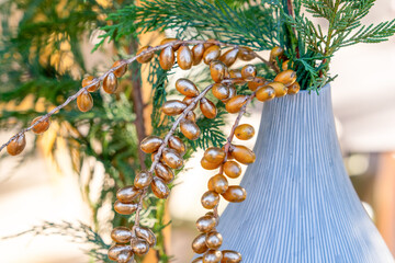 A close-up of shimmering golden berries and lush evergreen branches arranged in a textured grey vase, highlighting natural beauty and elegance.