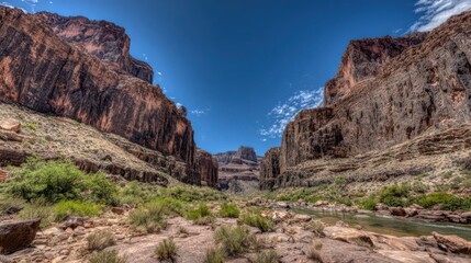 Fototapeta premium Vast canyon walls with sedimentary rock layers under a clear blue sky, showcasing ancient geological formations and rugged terrain.