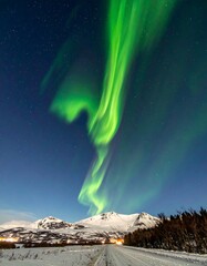 Spectacular green aurora borealis dances above snowy mountains at night