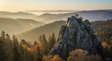 Rugged granite peak rises above densely forested hills bathed in early morning sunlight and haze