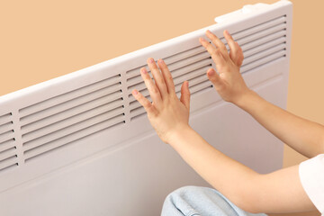 Little boy warming near electric convector heater on beige background, closeup