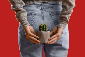 Young woman with hemorrhoids and cactus on red background, back view