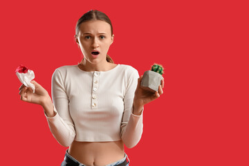Shocked young woman with cactus and bloody paper on red background. Hemorrhoids concept
