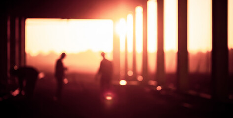 Silhouettes of people against bright sunset light through pillars, emphasizing scale, rhythm, and human movement within an unfinished architectural space