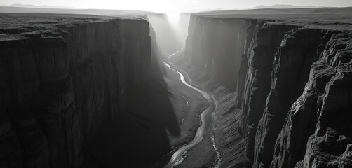 Deep dark canyon with steep rock walls and riverbed below. Light streams into narrow gorge creating dramatic shadows and immense depth. Serene wilderness scene in stark monochrome.