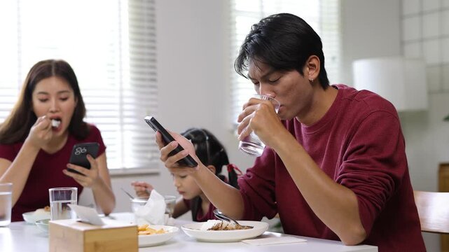Asian family ignoring each other using smartphones during dinner, the negative impact of smartphone addiction on family communication.