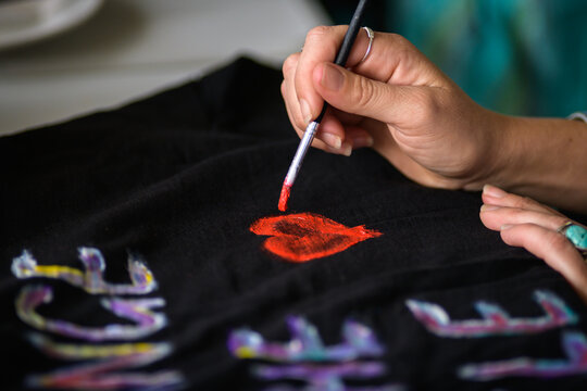 A hand holding a paint brush painting a red heart onto a tee shirt - horizontal