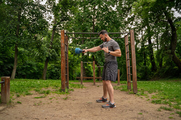 Handsome muscular man in his 40s using kettlebell side view,  healthy lifestyle concept, park workout 