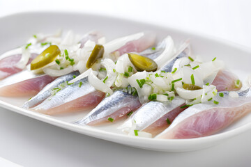 Gourmet Raw Herring with Onions and Pickles on a White Platter Styled in a Studio Setting
