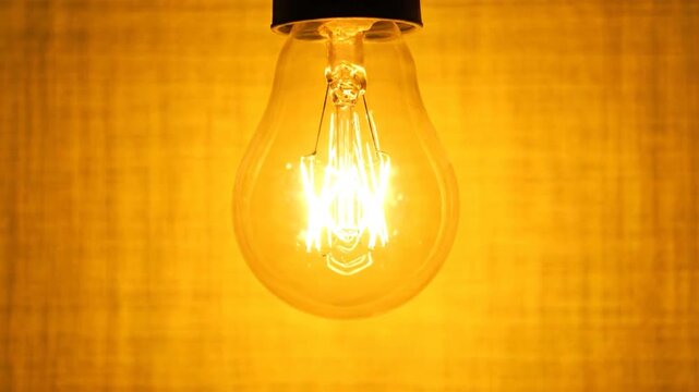 Lit bulb glows brightly against a textured yellow background, showcasing filament detail