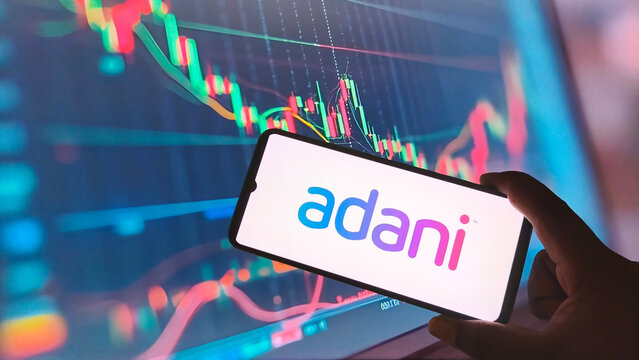 Adani logo on smartphone screen with stock market graph background