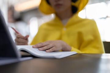 Asian student taking notes in notebook and using tablet for e-learning