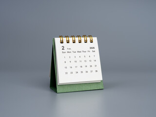 Green desk calendar showing February 2026, white page with a minimal design and angled perspective on a gray background. Ideal for time management, planning concepts, or business productivity visuals.