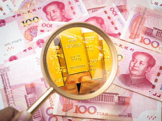 Gold bars under magnifying glass on Chinese Yuan banknotes. Concept of wealth, investment, China&rsquo;s economy, financial security, and asset diversification. Perfect for finance and global market themes.