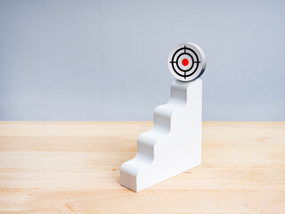 Minimal conceptual image of a white stair step rising to a 3d gun target icon on top, symbolizing achieving goals, business growth and success, personal development, and strategic progress.