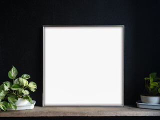 Mockup of a blank picture frame or canvas frame placed on a wooden shelf with green plants. Ideal for showcasing artwork, photography, or design in interior decoration and minimalist display scenes.