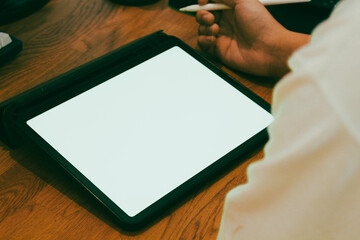 A businessman using digital tablet with blank white screen at wooden desk, productive work from home and remote office mockup concept.