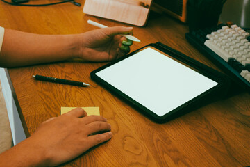 A businessman using digital tablet with blank white screen at wooden desk, productive work from home and remote office mockup concept.