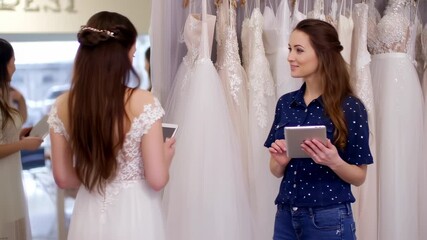 Two women in a bridal shop, using tablets, browsing dresses, interacting