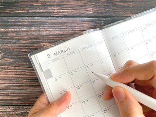 Woman's hand filling out a March schedule book on a wooden table