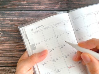 Woman's hand filling out April schedule book on wooden table