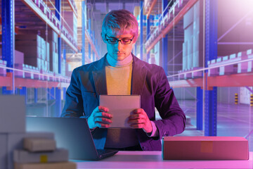 A warehouse manager inspects a package at a workstation, surrounded by boxes and a laptop, ensuring...
