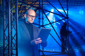 Stage engineering oversees assembly as an engineer monitors structural setup and lighting installation using a tablet while technicians work on the scaffold.