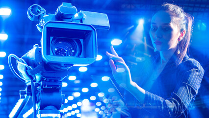 Video production control adjusts camera settings as a specialist configures recording parameters on a tablet amid bright studio lighting.