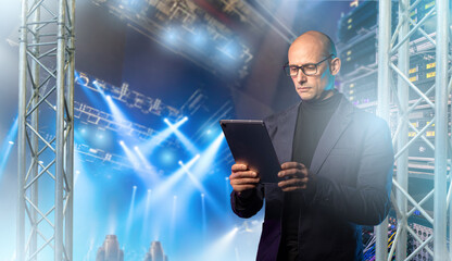 Stage production, event technician controls lighting and audio systems via tablet to manage live show equipment inside a professional concert venue.