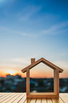 Wooden house frame model placed on table with blurred suburban background at sunset, symbolizing real estate planning, home construction, architecture design, housing development, and investment.