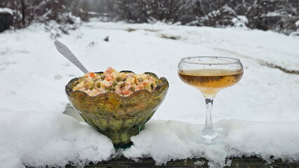 Olivier salad and a glass of champagne against a snowy backdrop