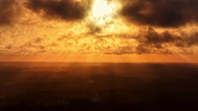 Dramatic golden-hour timelapse of clouds moving across the sky as sun rays break through, creating intense atmospheric light over a dark landscape.